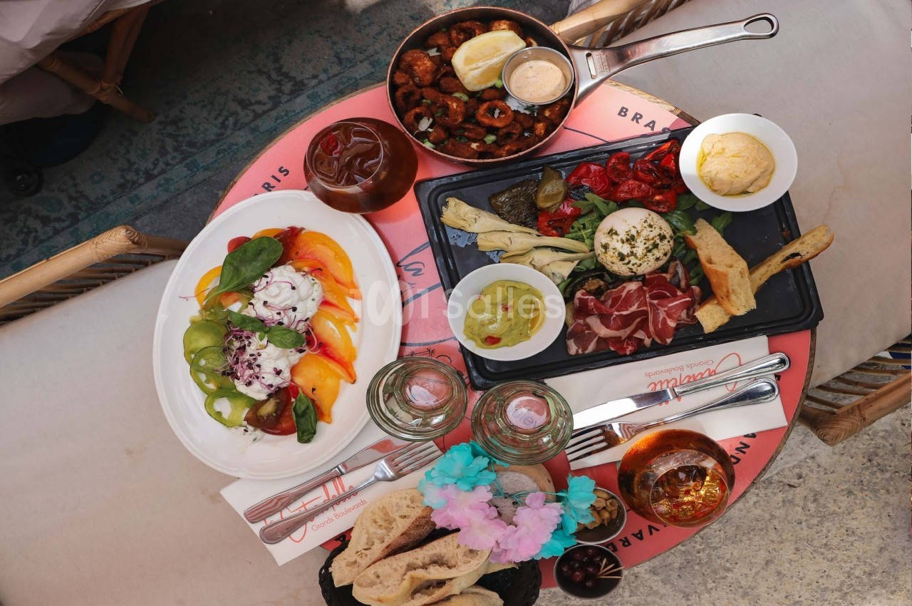 Assortiment de plats méditerranéens avec légumes, charcuterie, pain, sauces et boissons sur une table ronde.