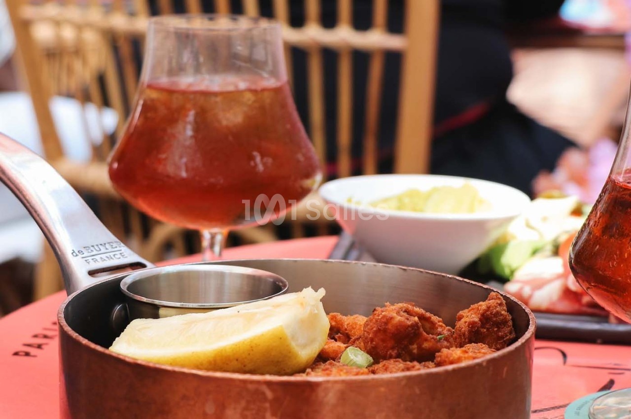 Plat de beignets servis dans une casserole en cuivre avec un quartier de citron, accompagné de boissons et d'accompagnements.