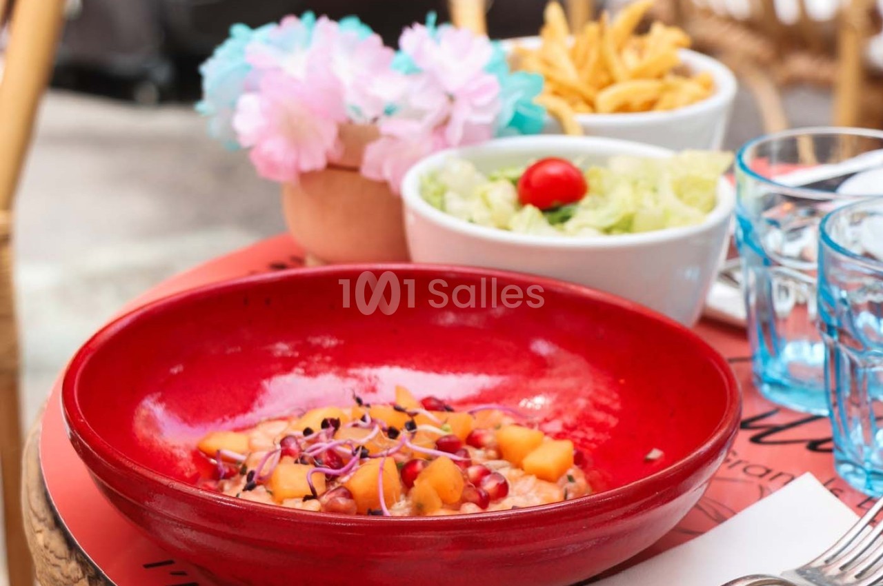 Assiette de salade colorée avec fruits et graines, accompagnée de frites et d'une salade verte sur une table en terrasse.