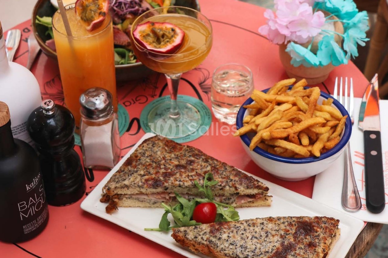 Assiette avec croque-monsieur, frites, salade, cocktails et condiments sur une table rouge décorée.
