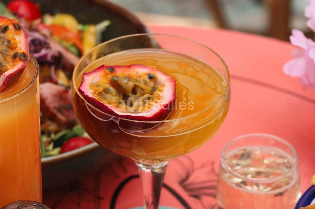 Cocktail servi dans une coupe avec un demi-fruit de la passion en garniture, posé sur une table rouge.