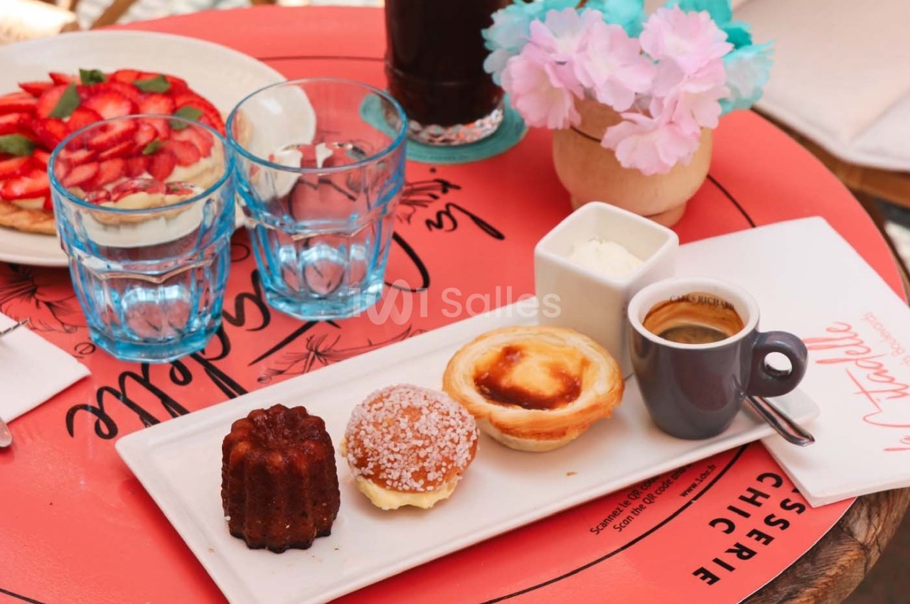 Plateau avec un café, un cannelé, une tartelette, une brioche, de la crème et des verres sur une table rouge.