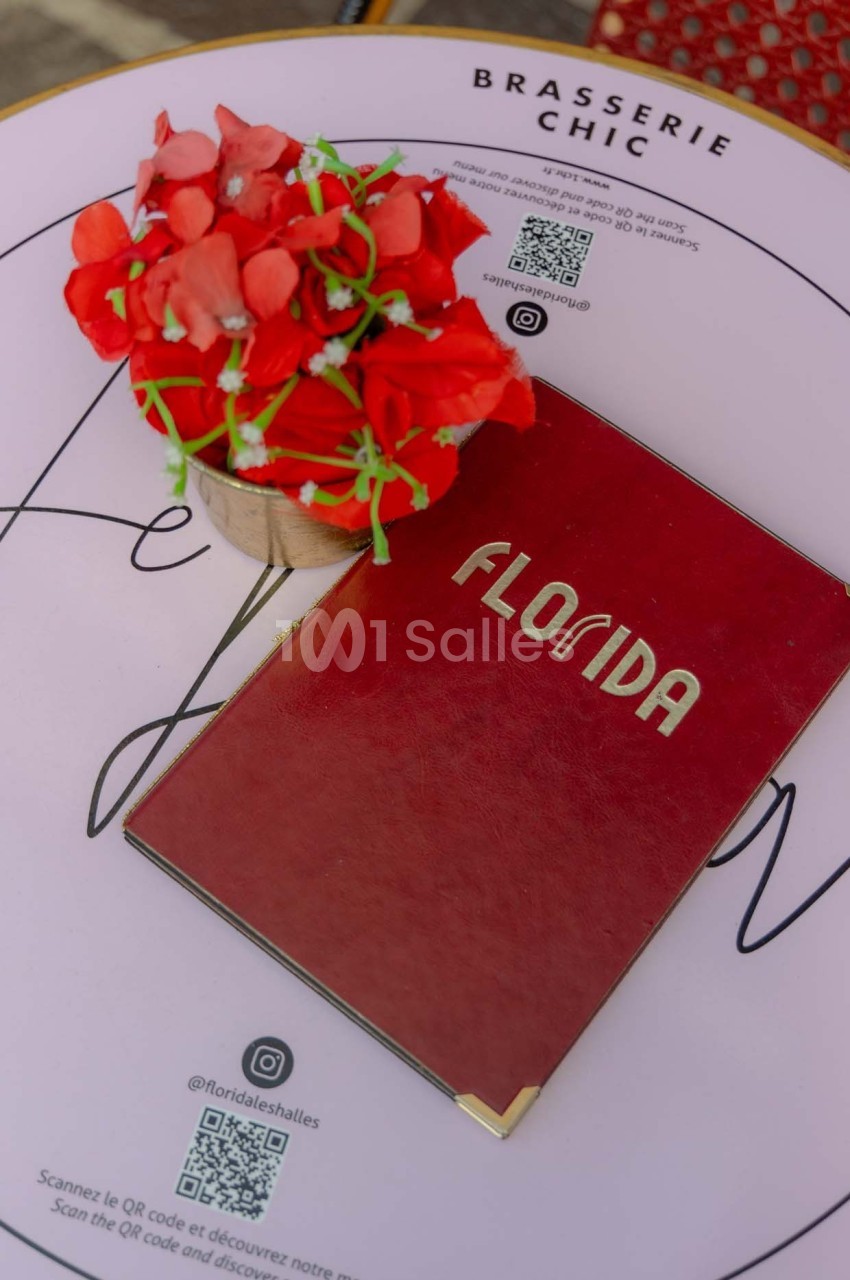 Menu rouge marqué ’Florida’ posé sur une table ronde blanche avec un bouquet de fleurs rouges et des QR codes imprimés.
