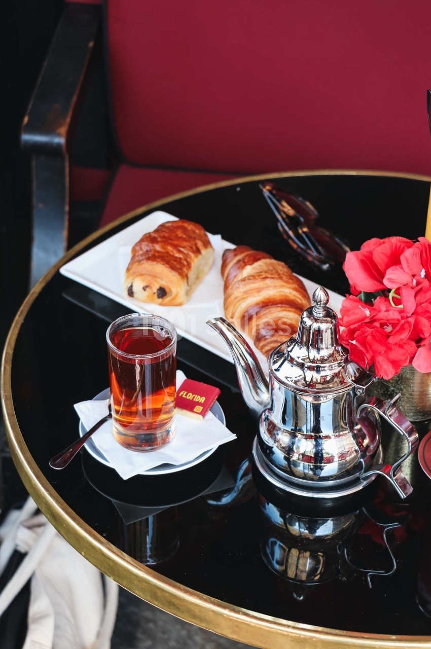 Petit-déjeuner avec thé, croissant, pain au chocolat et fleurs rouges sur une table noire dans un café.