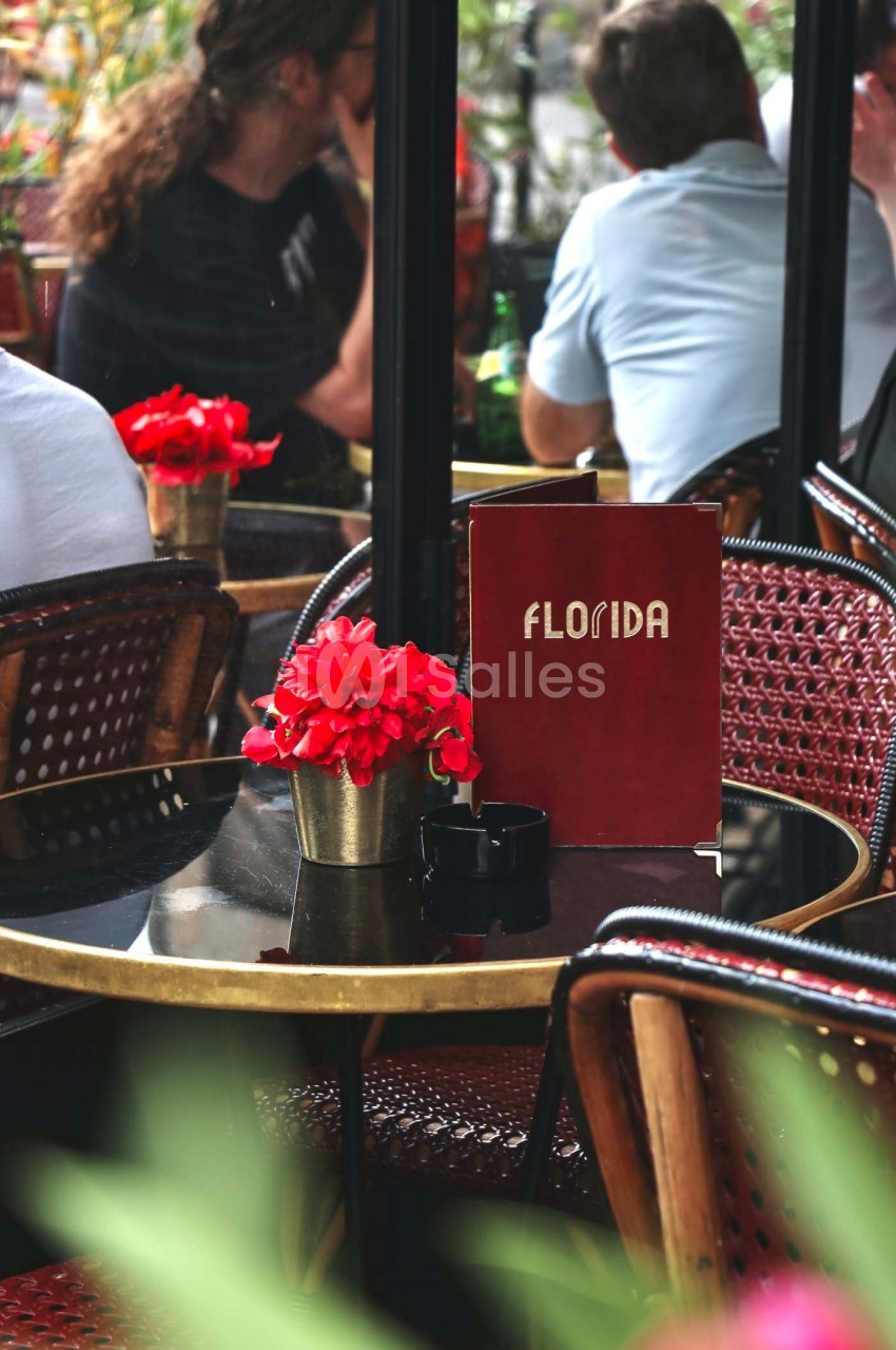 Des tables de café en terrasse avec des fleurs rouges et un menu rouge marqué ’Florida’ posé sur l'une d'elles.