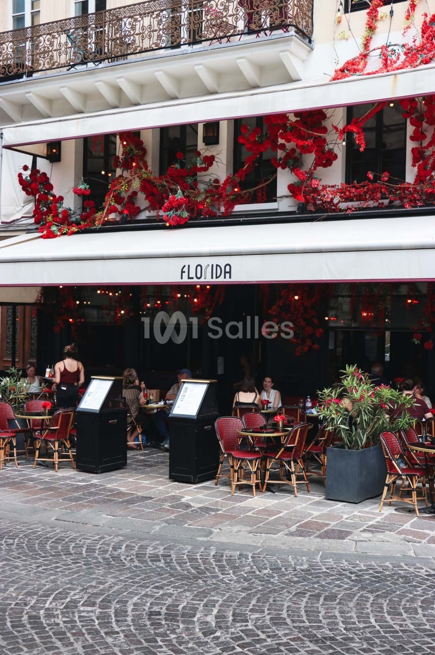 Terrasse d’un café-restaurant avec des tables occupées, façade ornée de fleurs rouges et enseigne ’Florida’.