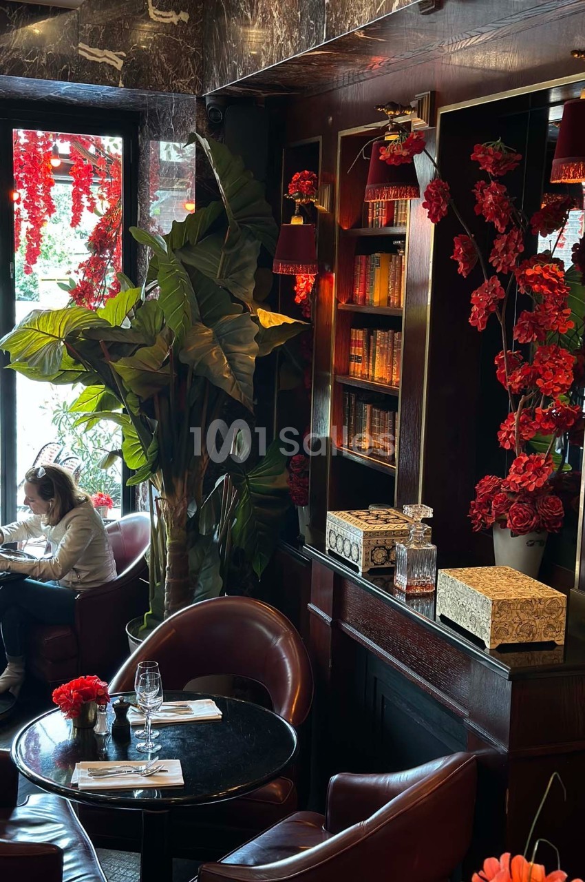 Intérieur d'un café élégant avec fauteuils en cuir, plantes, étagères décorées et lumière tamisée.