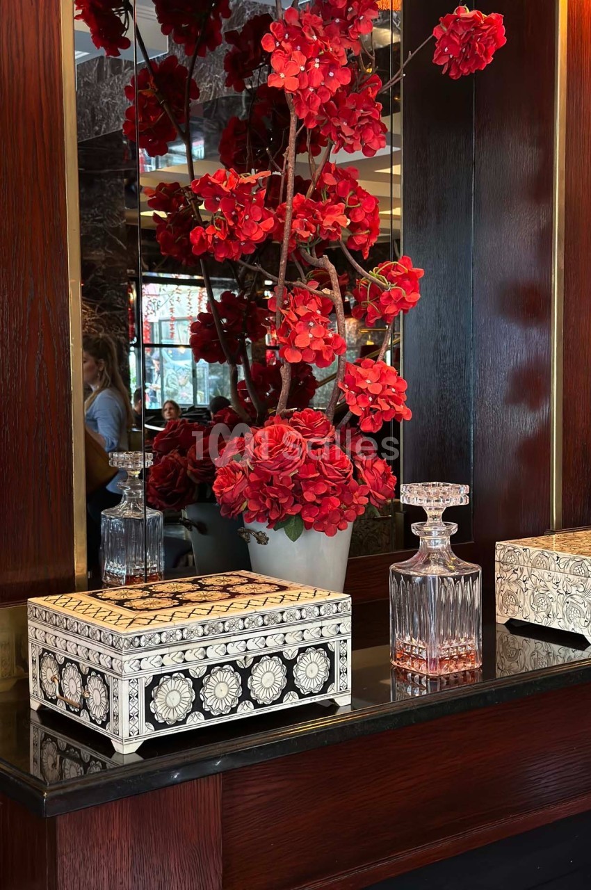 Vase de fleurs rouges avec des objets décoratifs en bois et en verre posés sur un meuble sombre.