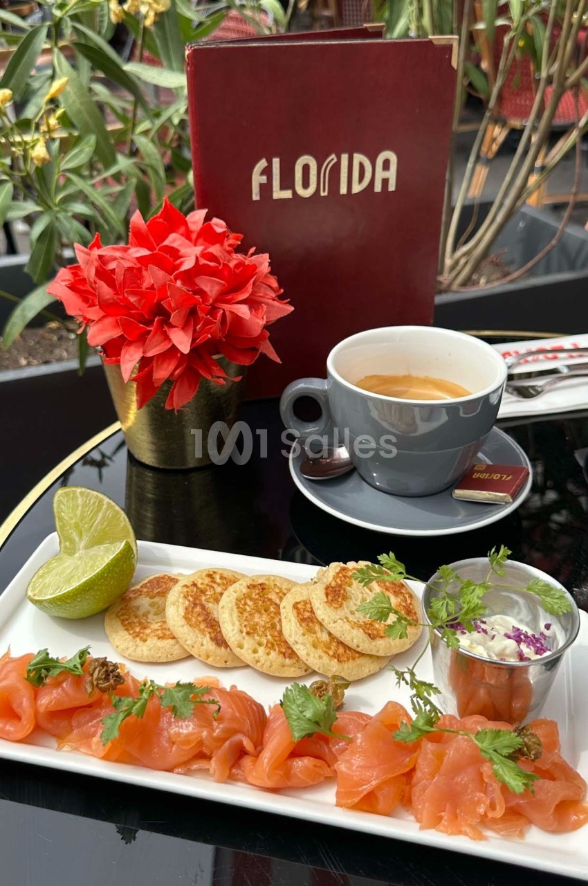 Assiette de saumon fumé, blinis, citron vert et crème, accompagnée d'un café sur une table de terrasse.