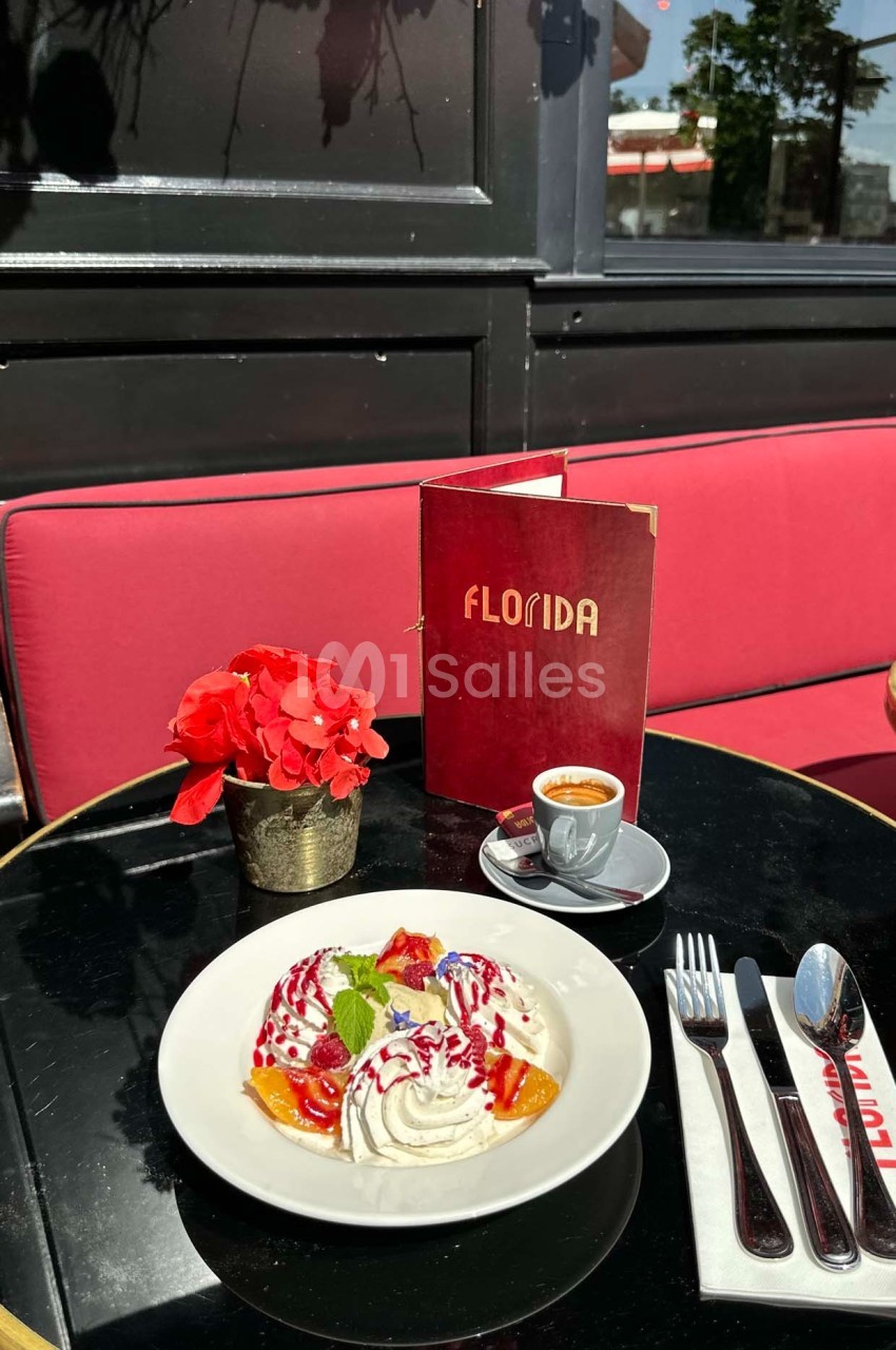 Dessert avec chantilly, fruits rouges et menthe, servi sur une terrasse avec un café, un menu et des fleurs rouges.