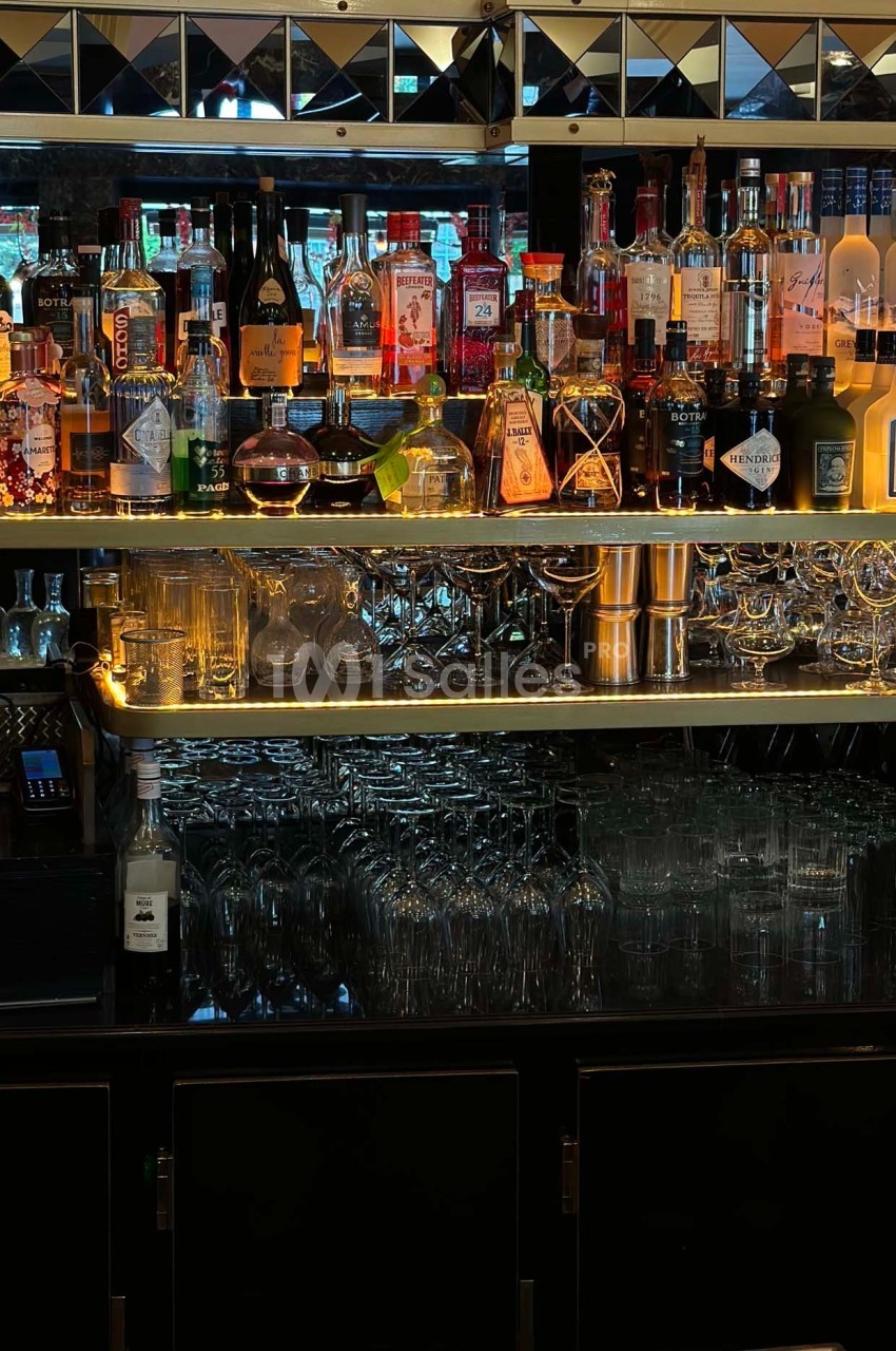 Étagères de bar avec une variété de bouteilles d'alcool, verres suspendus et éclairage tamisé.