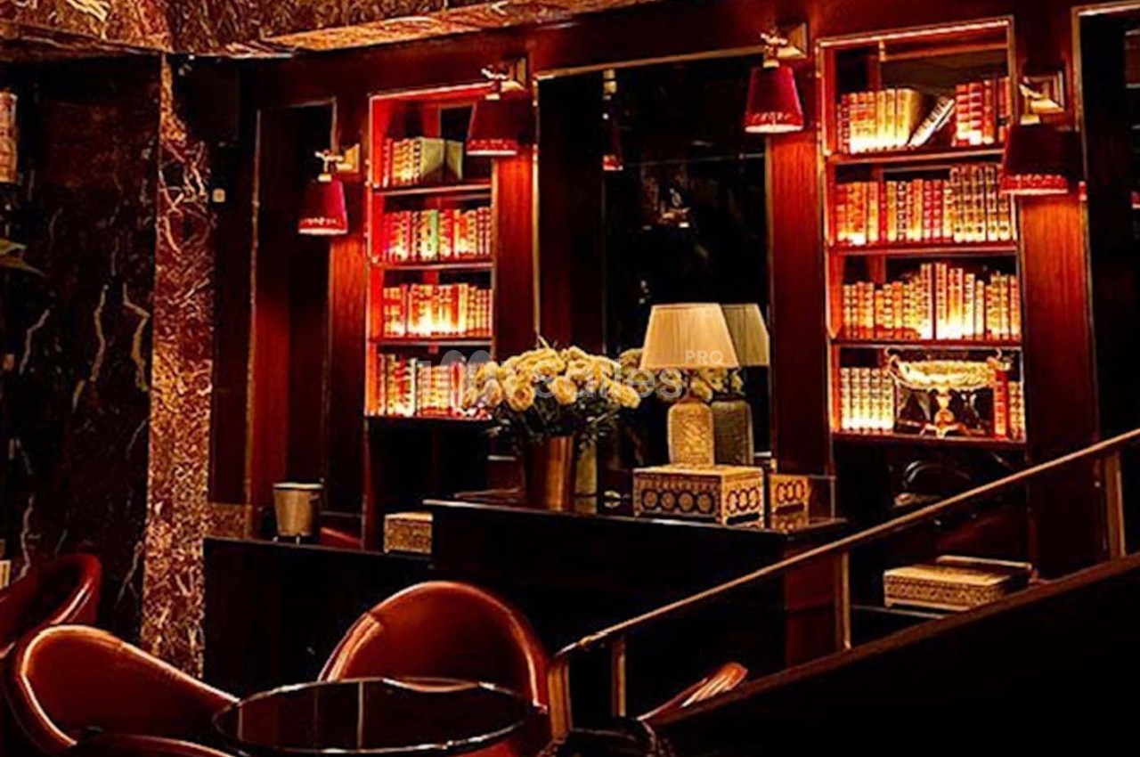 Bibliothèque éclairée avec des livres reliés, des lampes rouges et un bouquet de fleurs dans un intérieur chaleureux.