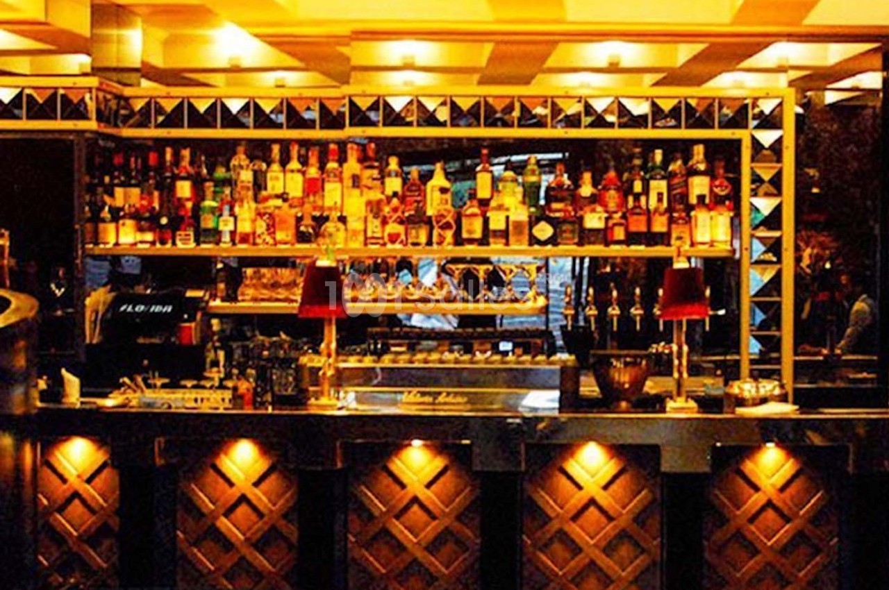 Bar éclairé avec des étagères remplies de bouteilles d'alcool, des lampes rouges et un comptoir en bois sculpté.