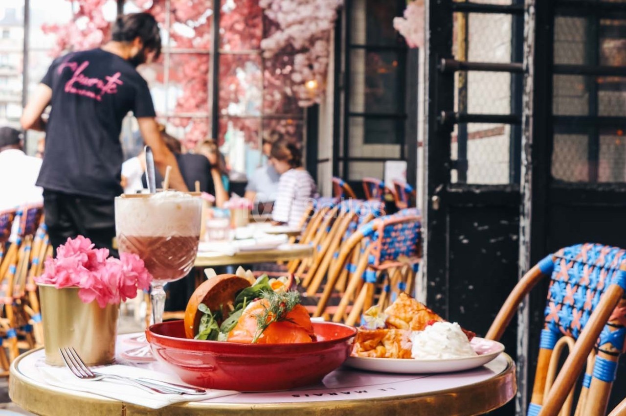 Repas servi en terrasse avec un bol de salade, une boisson et des fleurs roses en décoration sur la table.