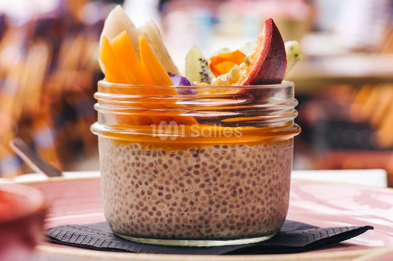Dessert aux graines de chia dans un bocal, garni de fruits frais colorés comme mangue, kiwi et pêche.