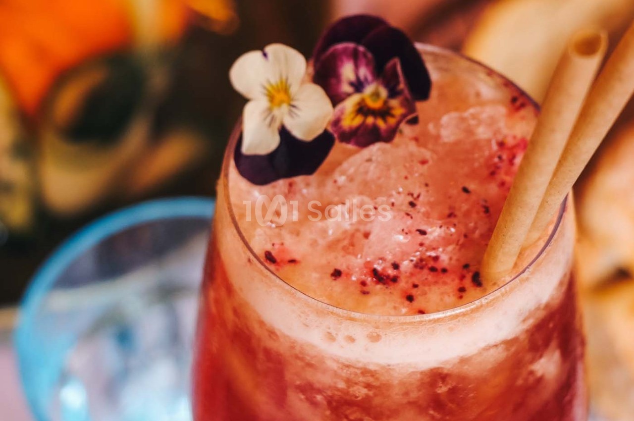 Boisson glacée rose garnie de fleurs comestibles et de pailles, servie dans un verre transparent.