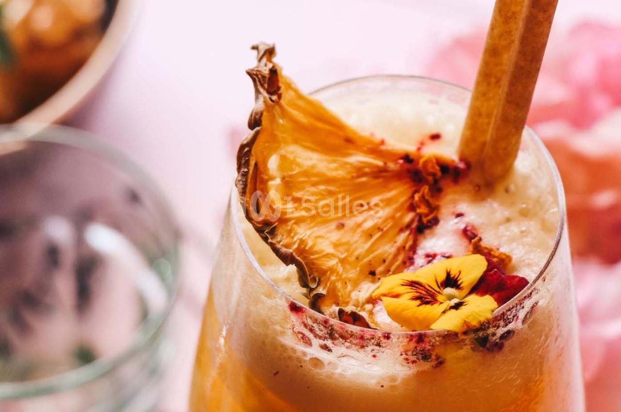 Boisson tropicale garnie d'une tranche d'ananas séchée et d'une fleur comestible, servie avec une paille.
