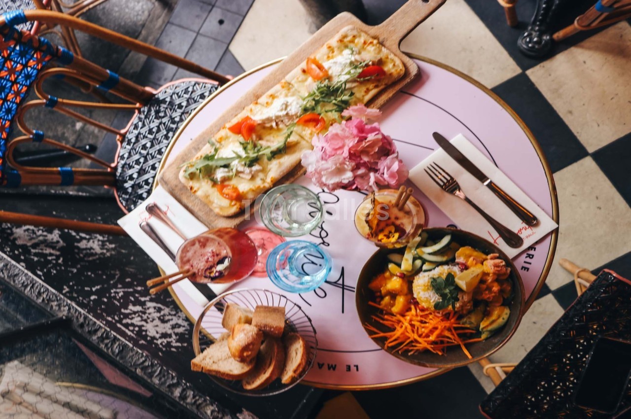 Table ronde avec des plats variés, dont une tarte fine, une salade colorée, du pain et des boissons, vue de dessus.