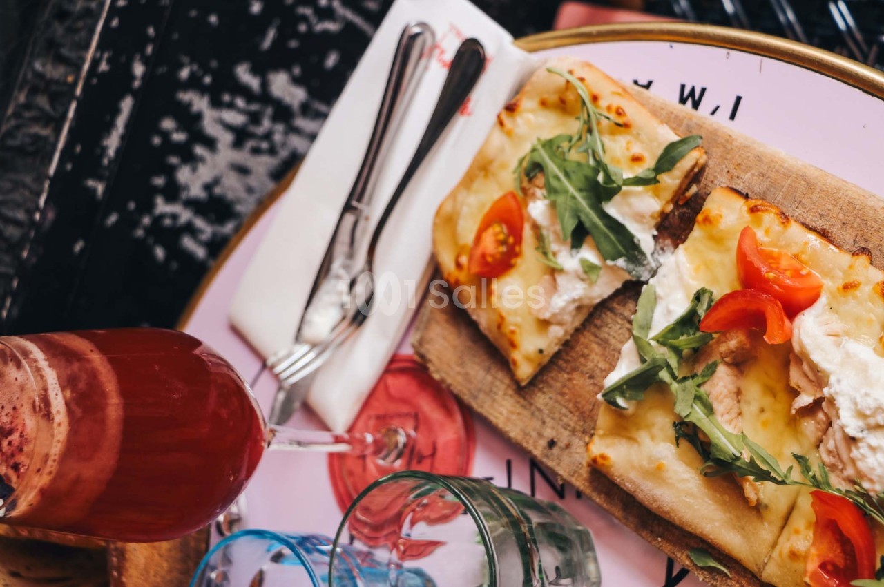 Deux parts de pizza garnies de roquette, tomates et fromage, servies sur une planche avec des couverts et un verre de…