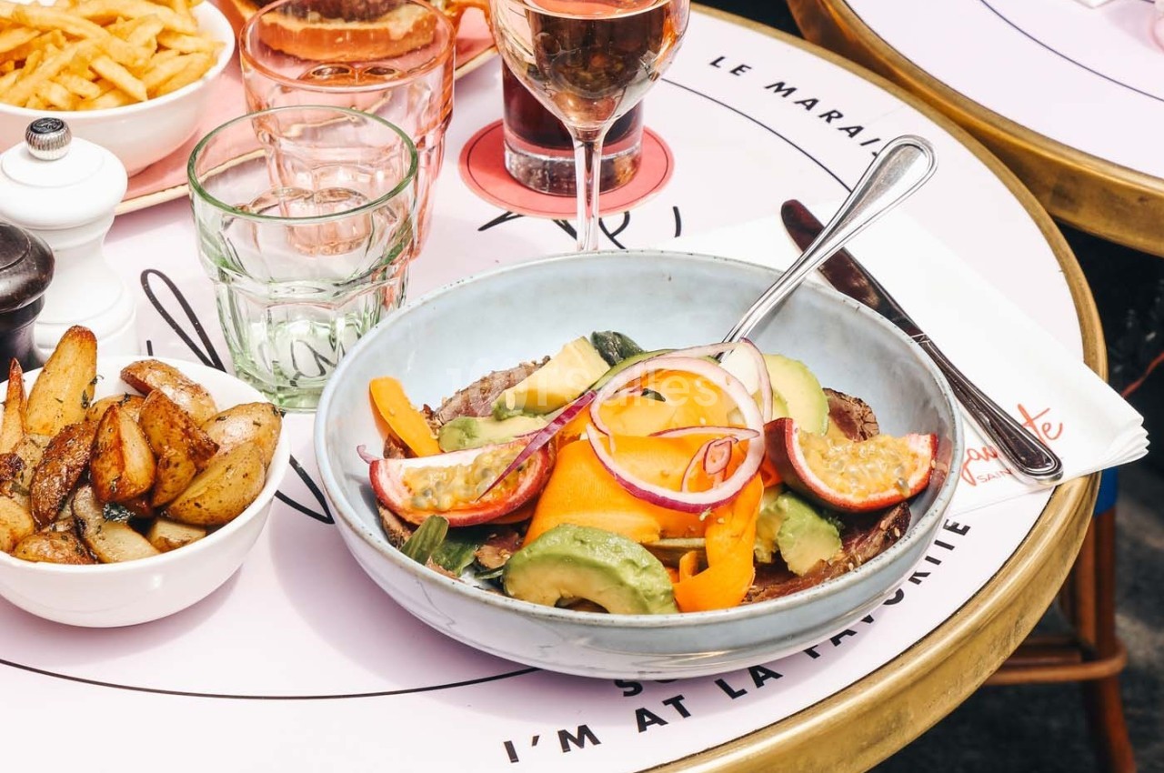 Assiette contenant une salade colorée avec légumes frais, avocat et viande, accompagnée de pommes de terre rôties.