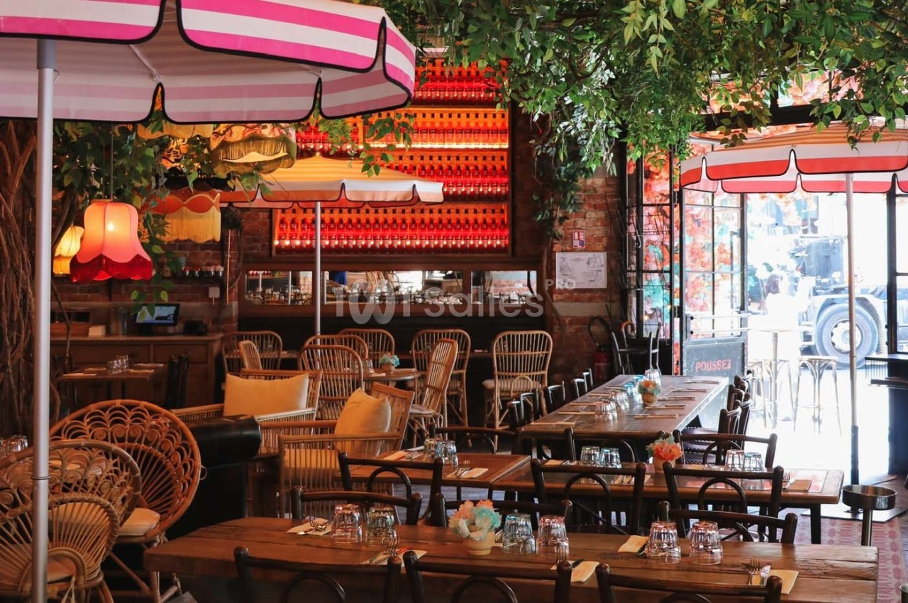 Salle de restaurant décorée avec des plantes suspendues, des lampes colorées et des tables en bois dressées.