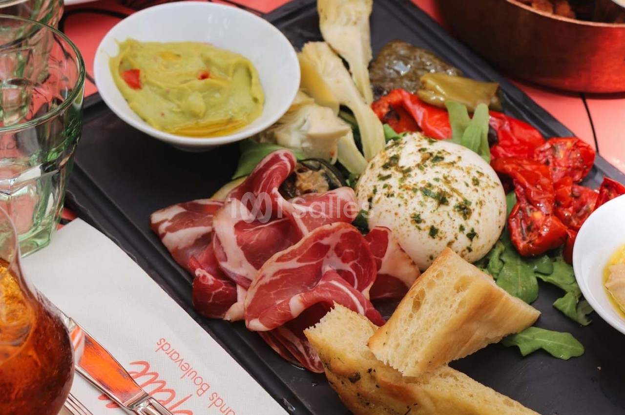 Assiette composée de burrata, charcuterie, légumes grillés, pain et guacamole, servie sur un plateau noir.