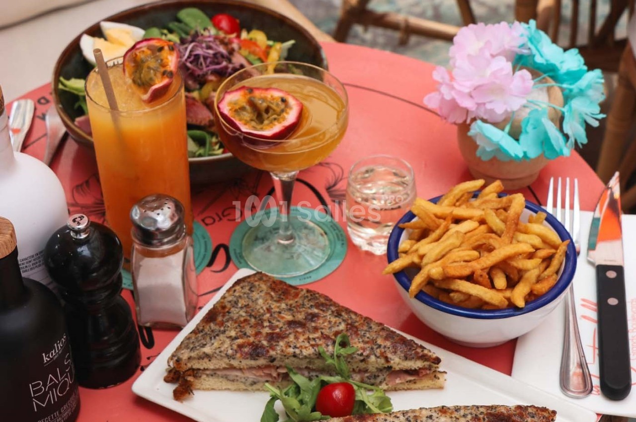 Assiette de croque-monsieur, frites, cocktails et salade sur une table colorée avec décorations florales.