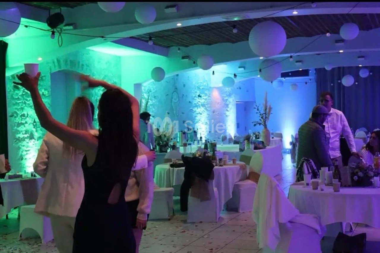 Salle de réception décorée avec des lanternes suspendues, éclairage coloré et invités en tenue de soirée.