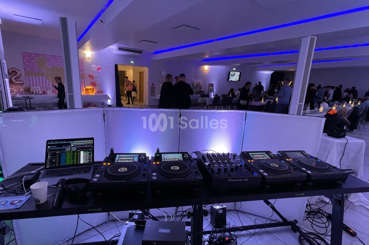 Matériel de DJ installé sur une table dans une salle éclairée, avec des invités rassemblés en arrière-plan.