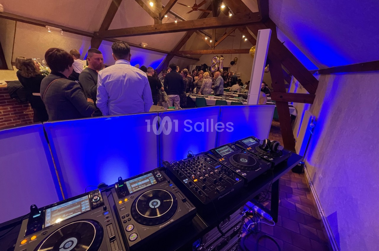 Platines DJ en premier plan dans une salle éclairée, avec des invités rassemblés en arrière-plan.