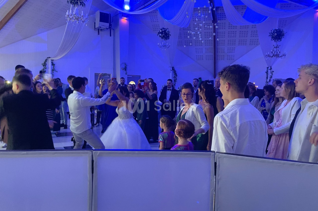 Groupe de personnes dansant lors d'une réception dans une salle décorée avec des drapés et un éclairage bleu.