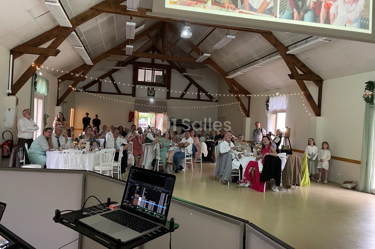 Invités assis dans une salle de réception décorée, regardant une projection lors d'un événement festif.