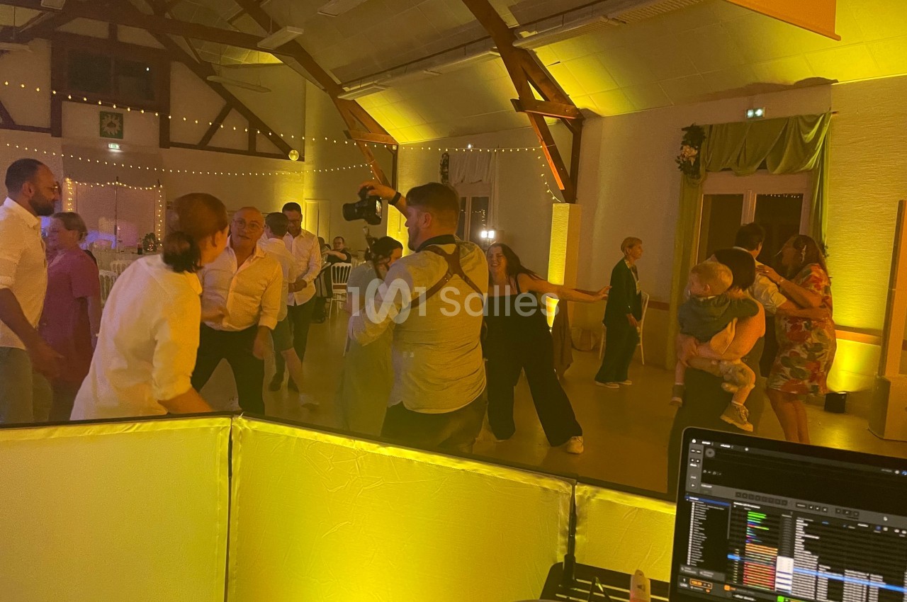 Des personnes dansent et discutent dans une salle éclairée de lumières jaunes, avec un DJ en arrière-plan.