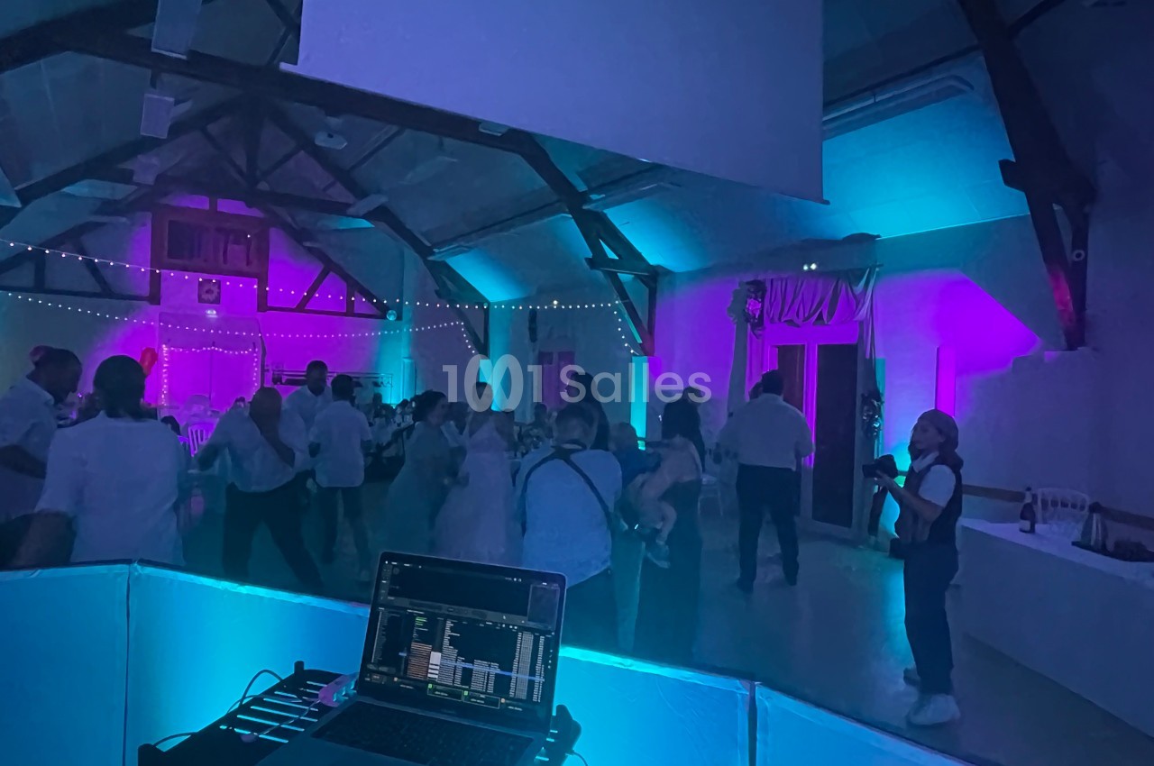 Des personnes dansent dans une salle éclairée par des lumières colorées, avec un ordinateur de DJ au premier plan.