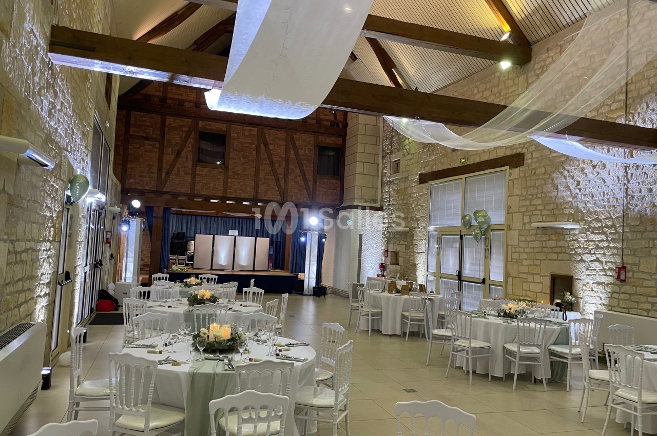 Salle de réception lumineuse avec murs en pierre, poutres apparentes, tables rondes dressées et décorations élégantes.