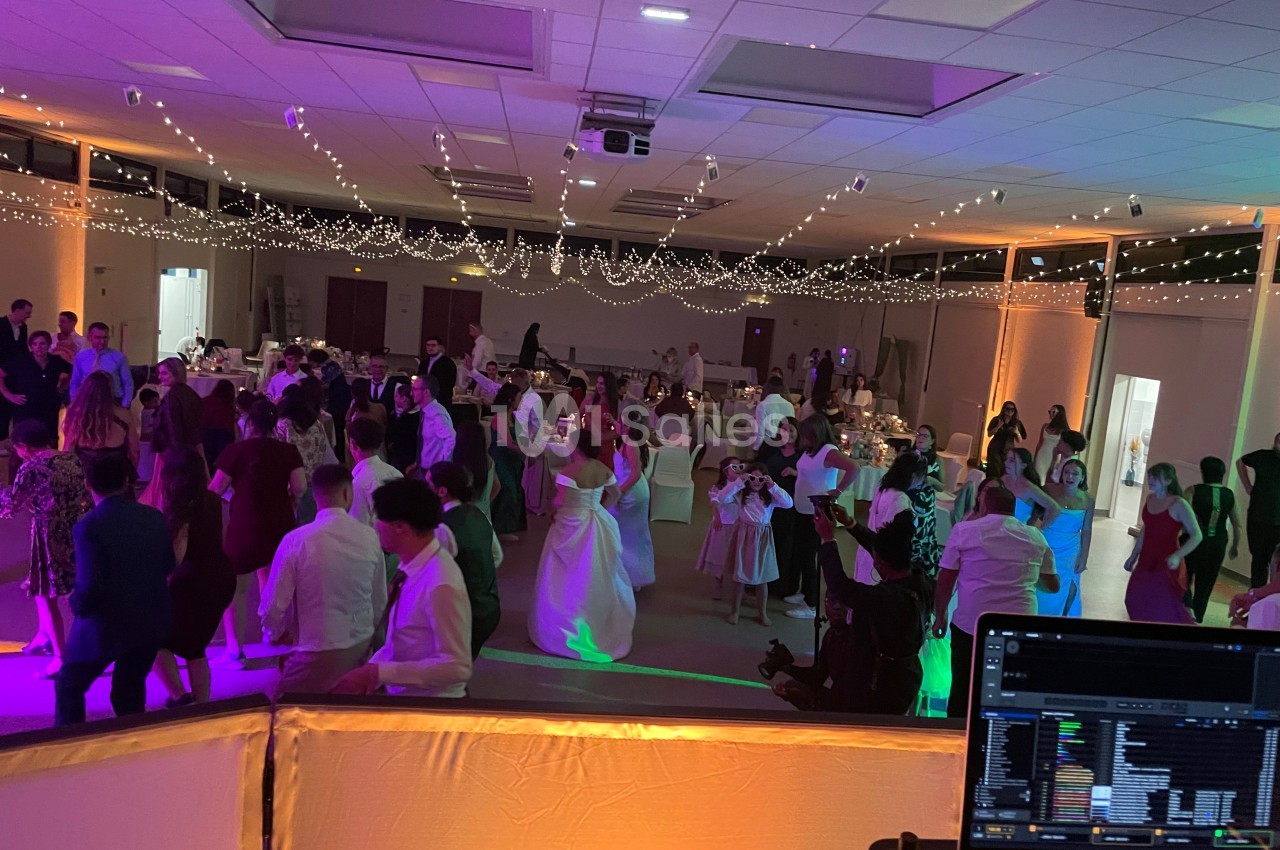 Salle de réception décorée avec des guirlandes lumineuses, des invités dansant sur une piste animée par un DJ.