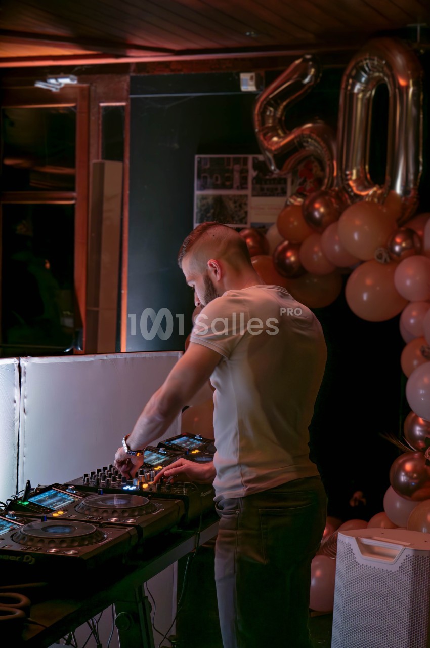 Un DJ mixe de la musique sur une table de mixage dans un décor festif avec des ballons et le chiffre 50 en arrière-plan.