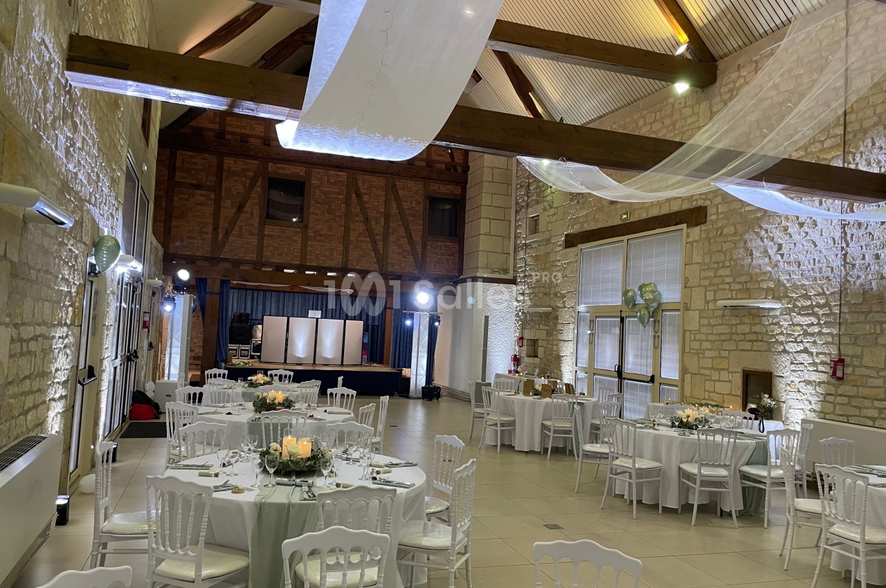 Salle de réception lumineuse avec murs en pierre, poutres apparentes, tables rondes dressées et décorations élégantes.