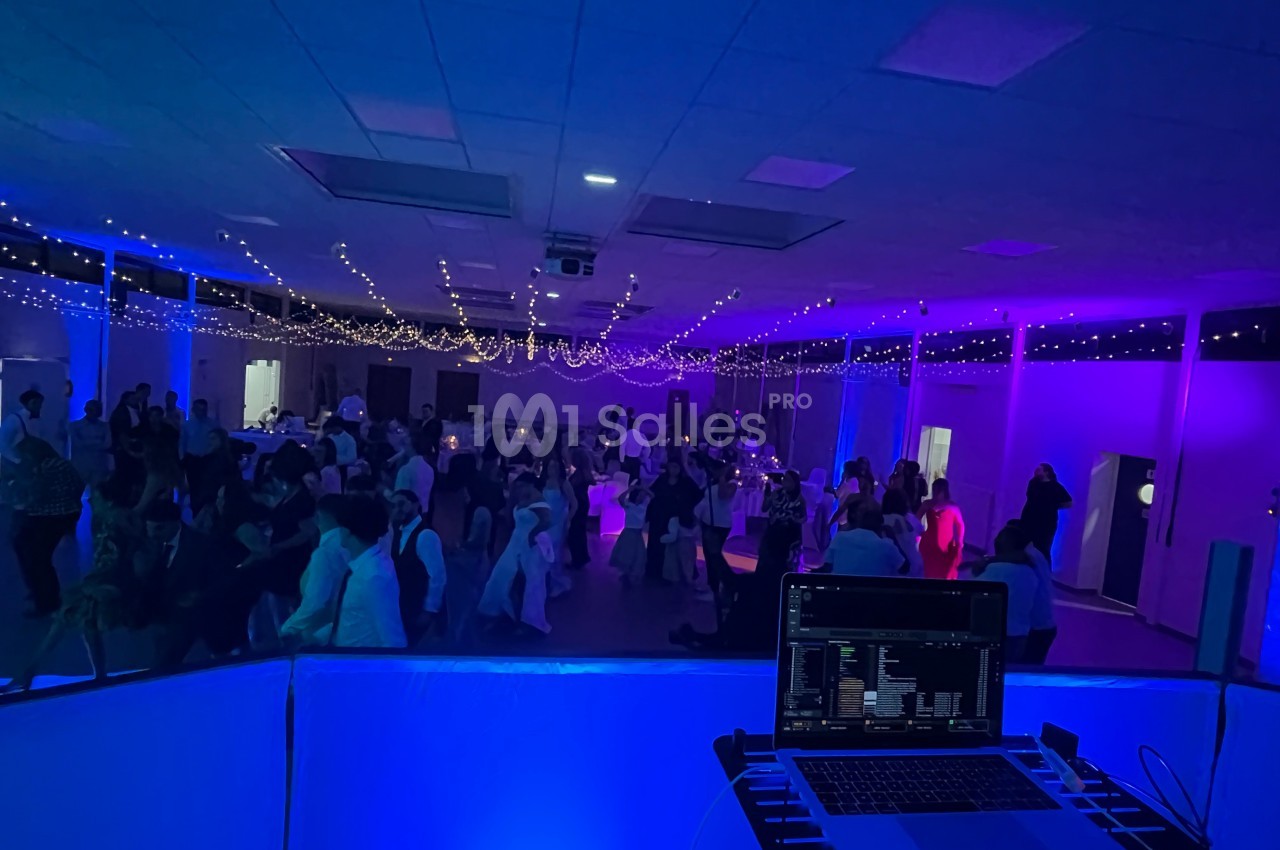 Salle de réception éclairée de lumières colorées, avec des invités dansant et un poste de DJ au premier plan.