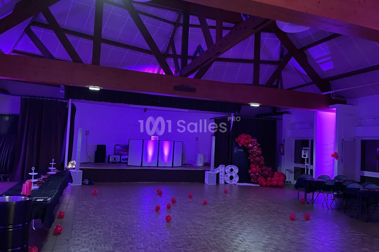 Salle décorée pour une fête avec éclairage violet, ballons rouges formant le chiffre 18 et espace de danse dégagé.