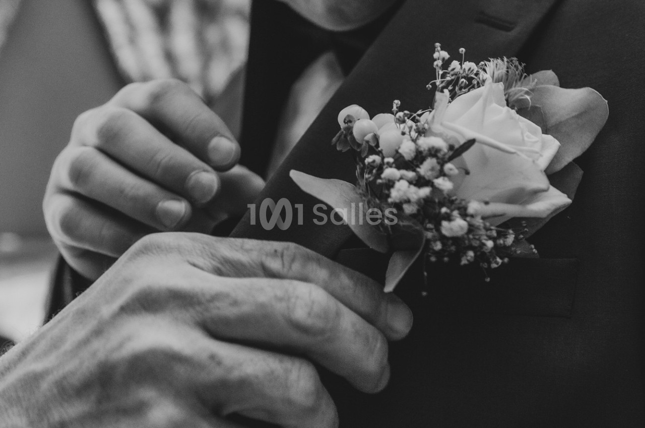 Un homme ajuste une boutonnière composée d'une rose et de petites fleurs blanches sur une veste sombre.