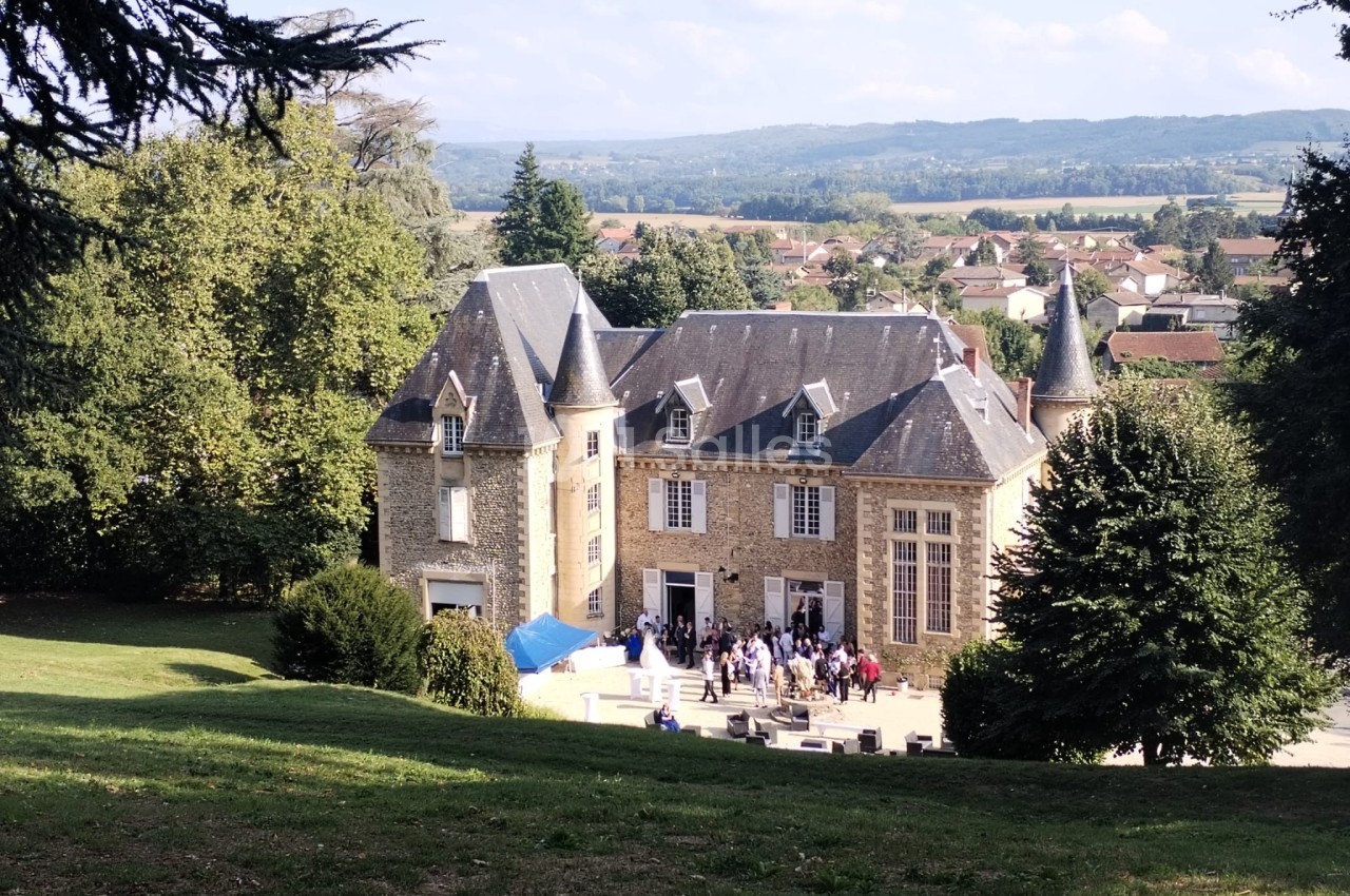 Vue d'un château en pierre entouré de verdure, avec des visiteurs rassemblés devant l'entrée par une journée ensoleillée.