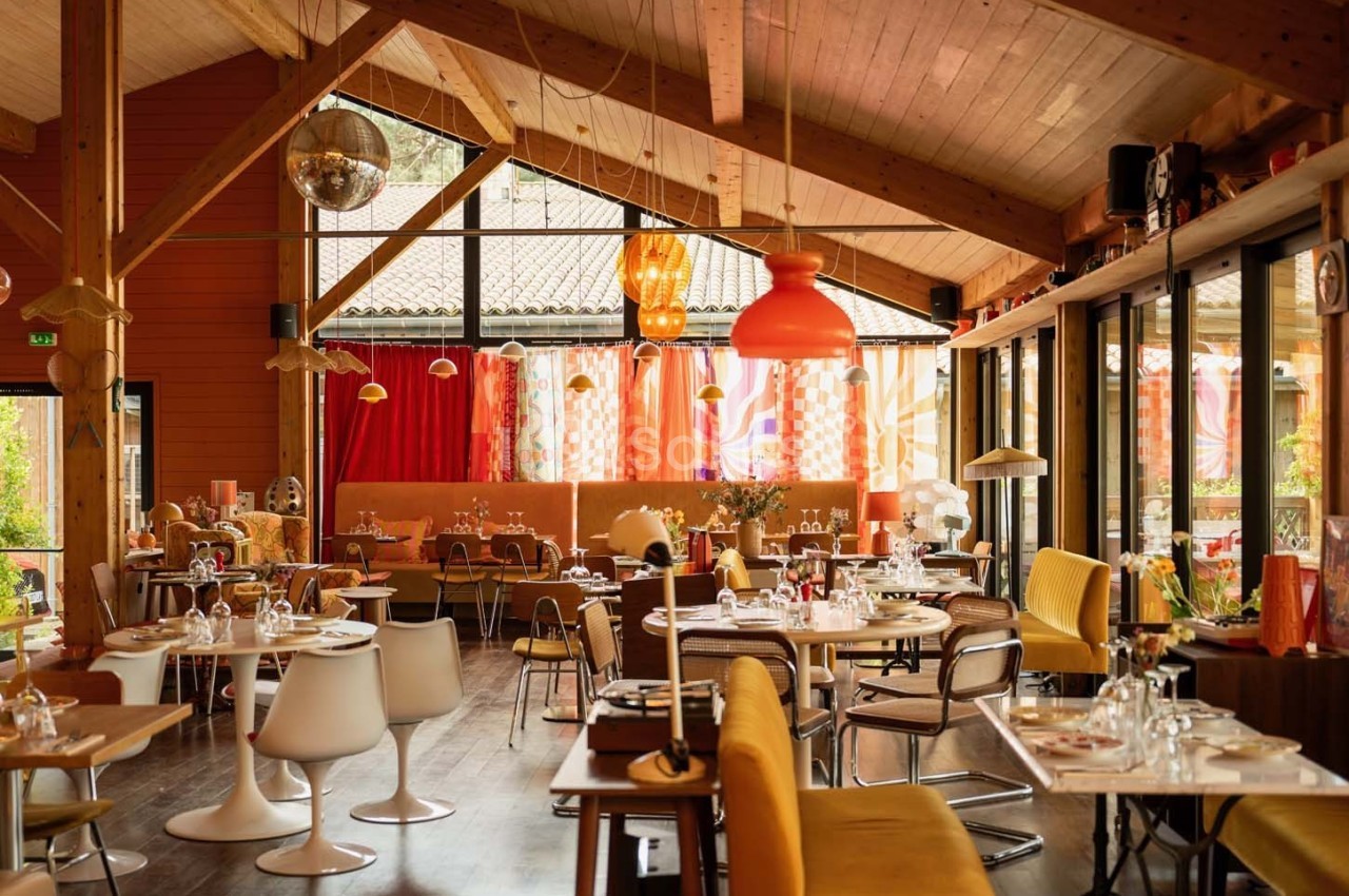 Salle de restaurant lumineuse avec décoration colorée, mobilier varié et grandes baies vitrées donnant sur l'extérieur.