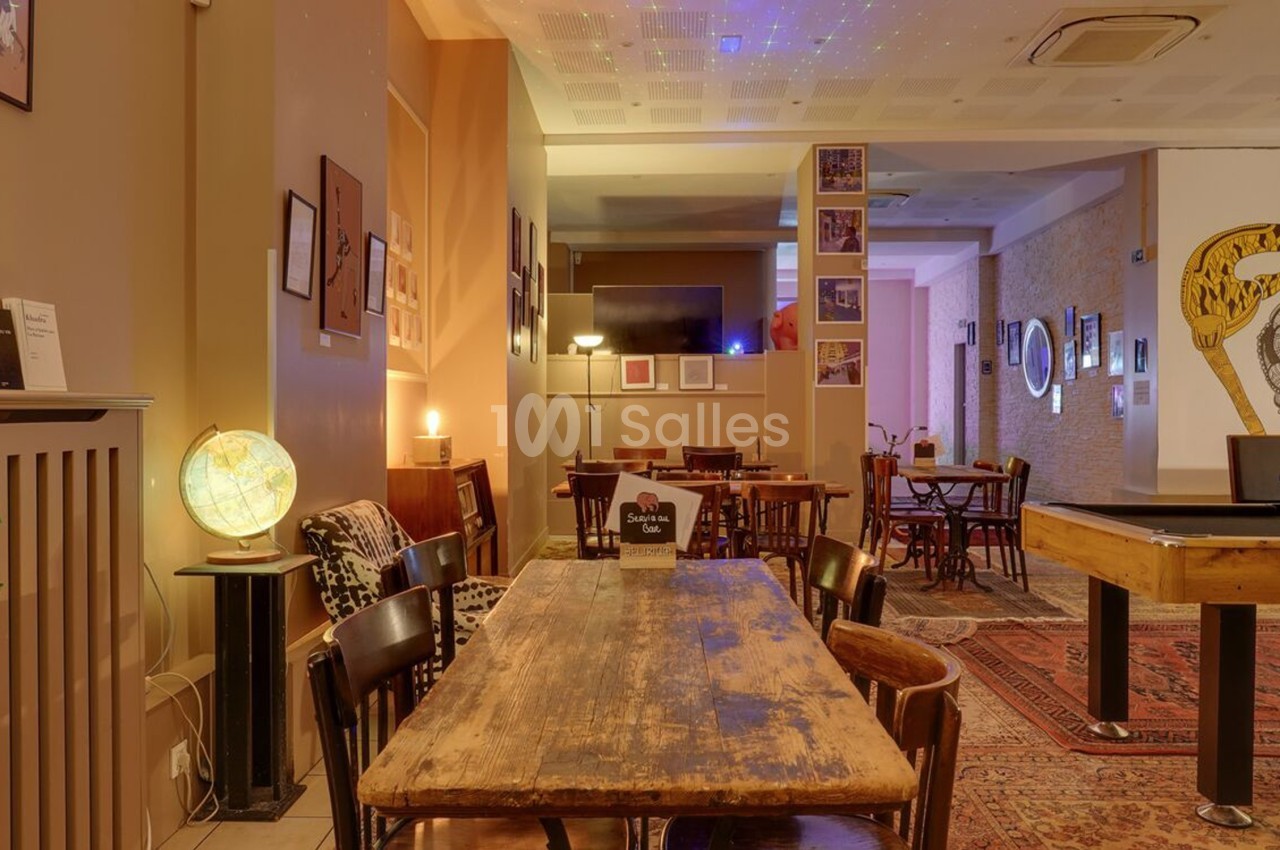 Salle chaleureuse avec tables en bois, chaises, globe lumineux et décorations murales dans une ambiance tamisée.