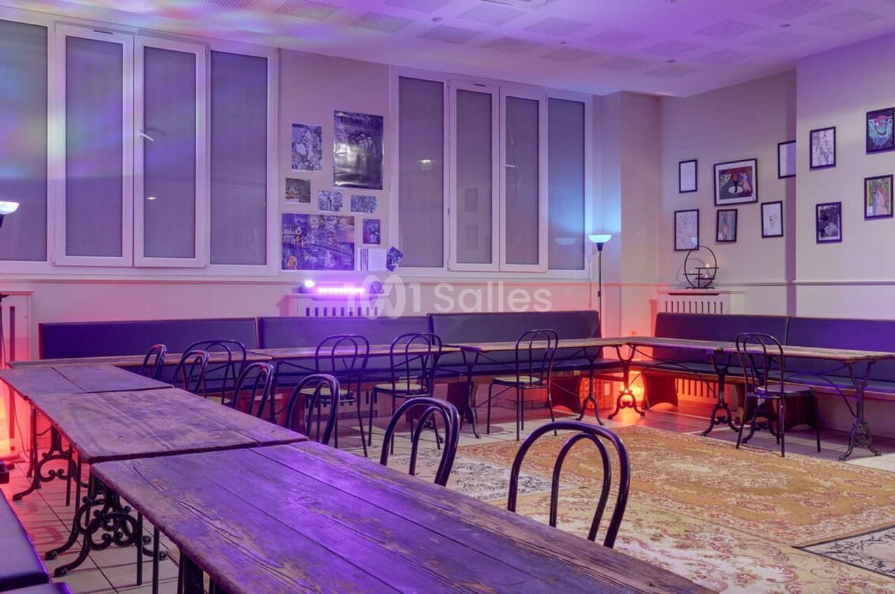 Salle lumineuse avec tables en bois, chaises noires, murs décorés de cadres et éclairage coloré.