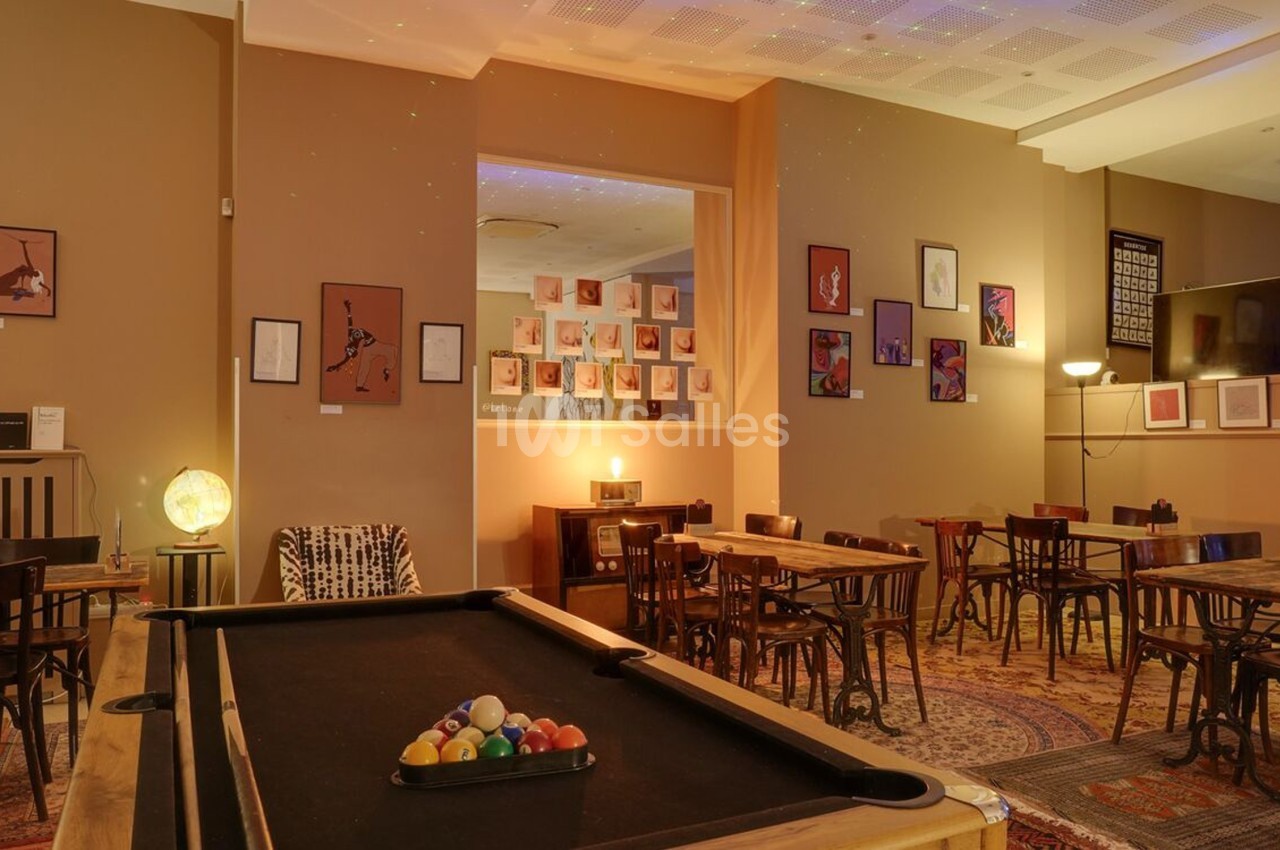 Salle chaleureuse avec tables en bois, billard au premier plan, décorations murales et éclairage tamisé.