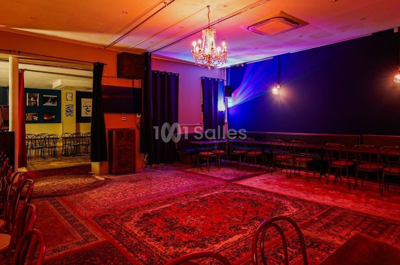 Salle avec tapis colorés, chaises alignées, murs sombres, éclairage tamisé et lustre central.