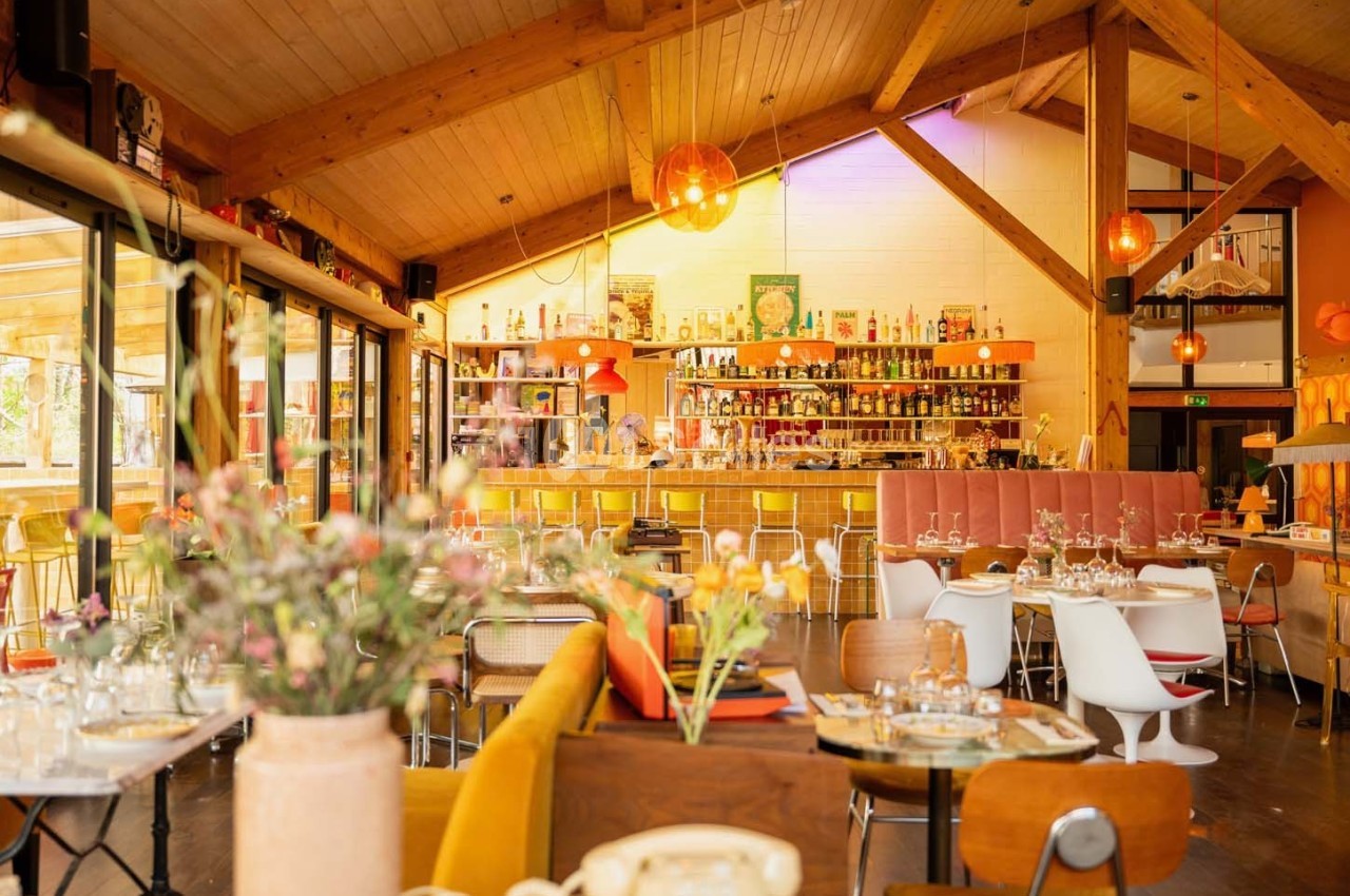 Salle de restaurant lumineuse avec une décoration chaleureuse en bois, tables dressées et un bar en arrière-plan.