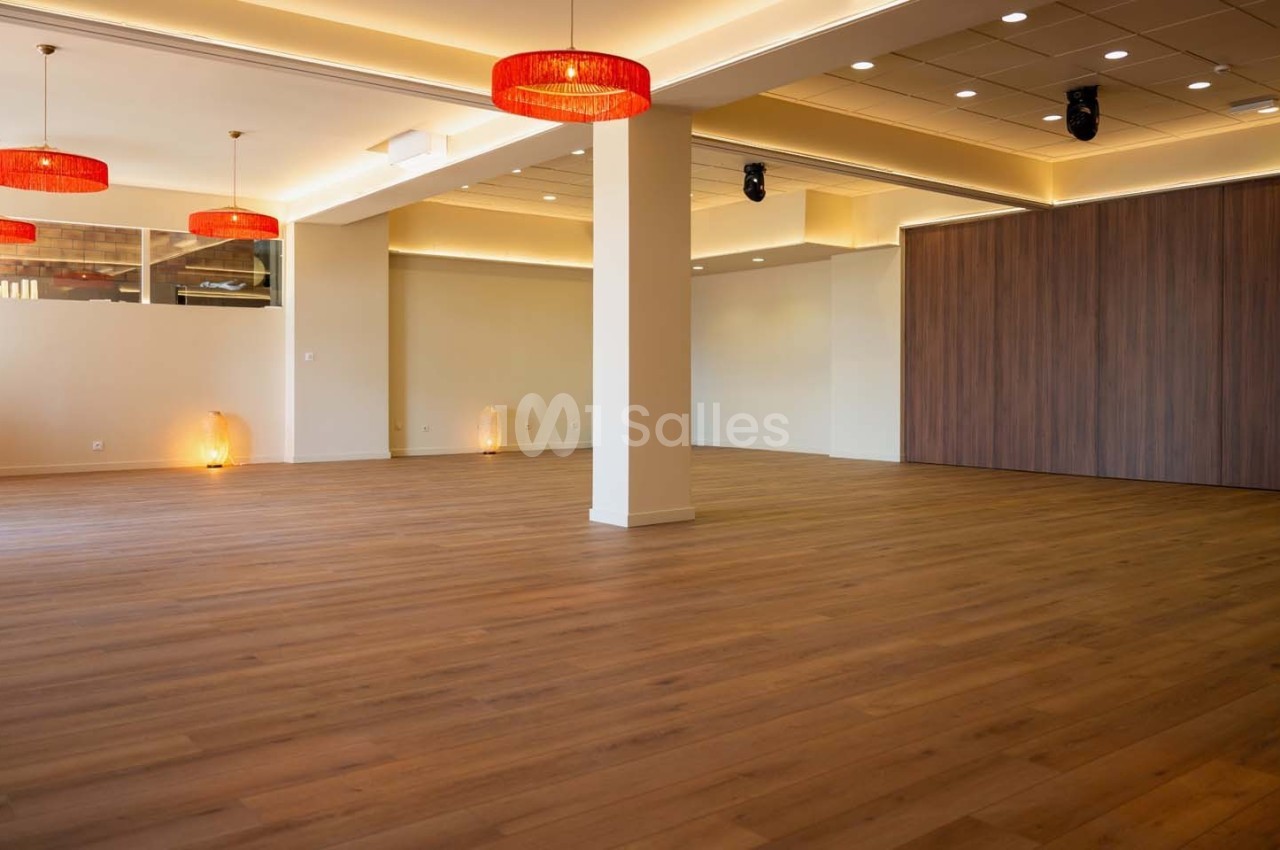 Salle spacieuse avec parquet en bois, murs clairs, éclairage suspendu et panneaux en bois sombre.