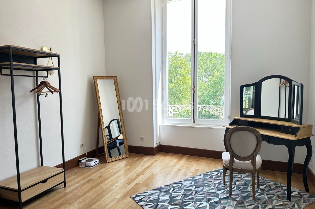 Chambre lumineuse avec coiffeuse, miroir sur pied, portant en métal et parquet en bois clair.